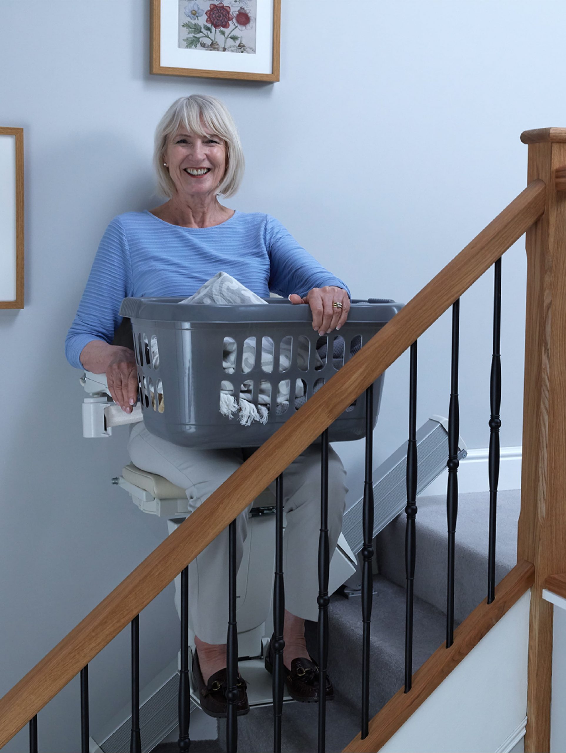 Femme avec un panier à linge montant des marches en utilisant un monte-escalier Handicare